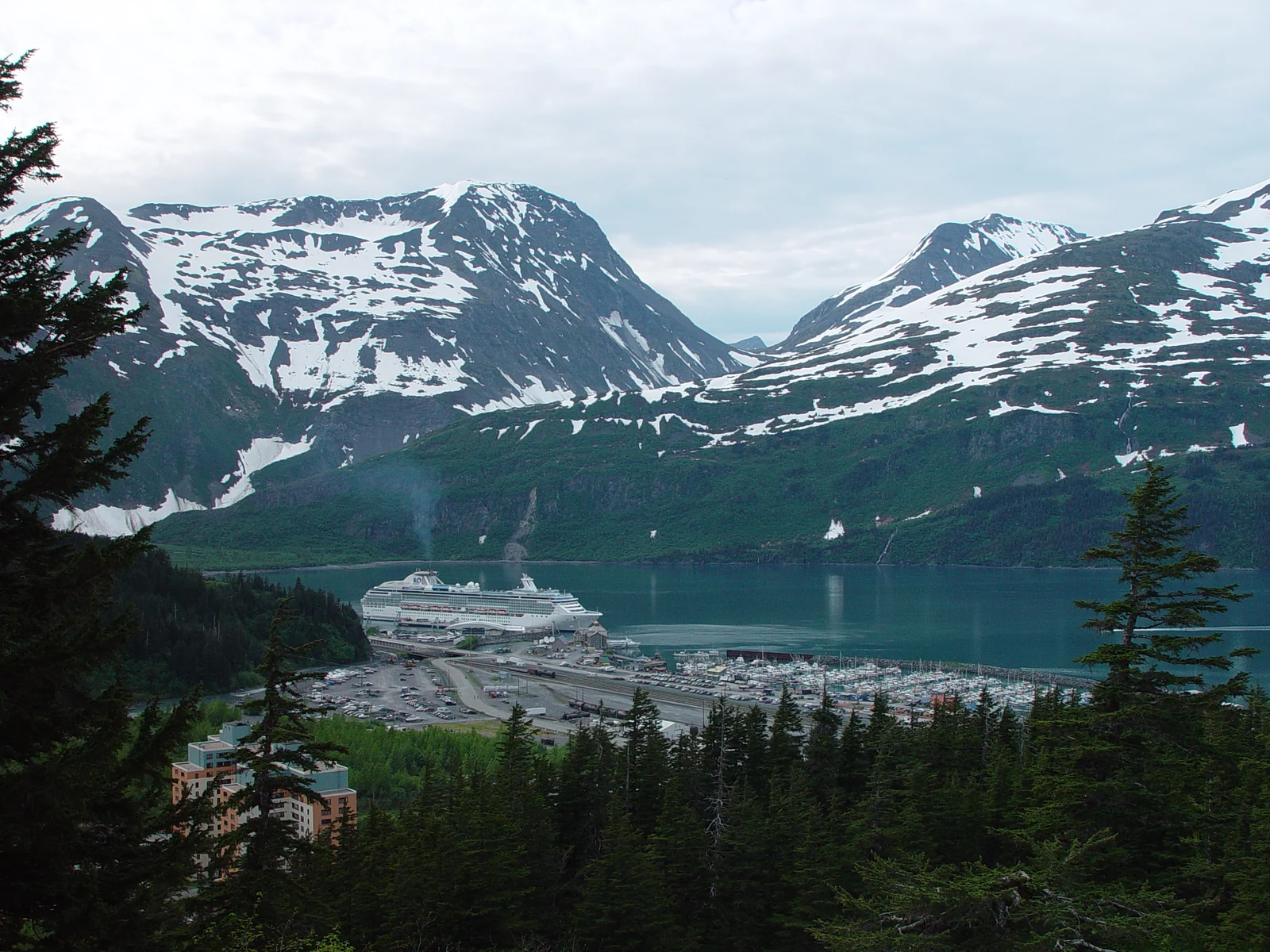 Archival view of Whittier, Alaska, with a cruise ship, harbor and snow-streaked mountains in June 2004